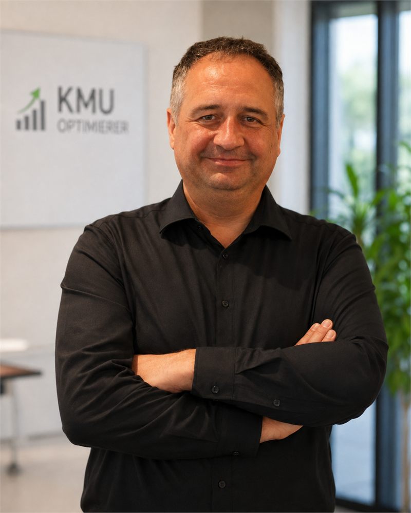 Thomas Krauß mit verschränkten Armen in seinem Büro, im Hintergrund das Logo des KMU-Optimierers